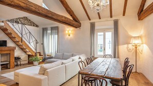 A spacious living area with a wooden dining table, a sofa, and a staircase.