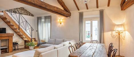 A spacious living area with a wooden dining table, a sofa, and a staircase.