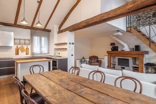 A rustic interior with exposed wooden beams, a stone fireplace, a dining area with a wooden table, and a kitchen with modern appliances. - Como Dreamhouse (Como)