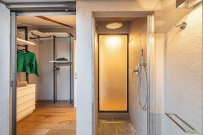 A narrow hallway leading to a bathroom with a shower, a towel rack, and a shelf with a green garment. - Como Dreamhouse (Como)