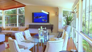 A modern living room with a glass coffee table, white upholstered sofas, and a large TV mounted on the wall.