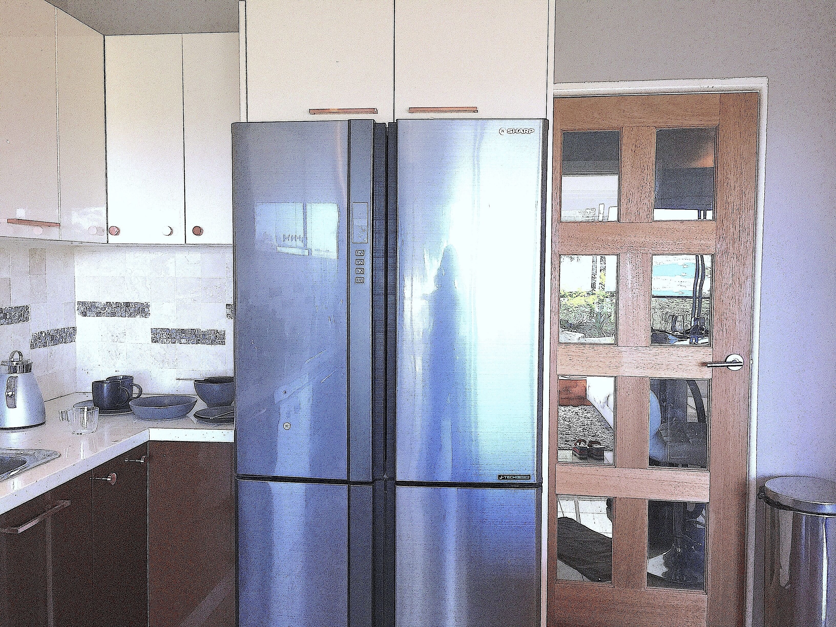 A kitchen with a double-door refrigerator, cabinets, and a window with a view.