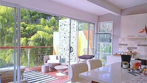 A modern kitchen with white cabinets, a large island, and a view of lush greenery through large sliding glass doors.