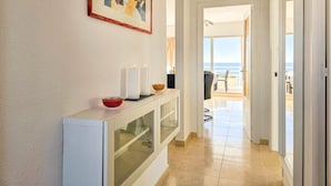 A hallway with a white console table, a framed abstract painting, and a view of the ocean through an open door. - Two bedroom apartment in Riviera del Sol (Mijas Costa)