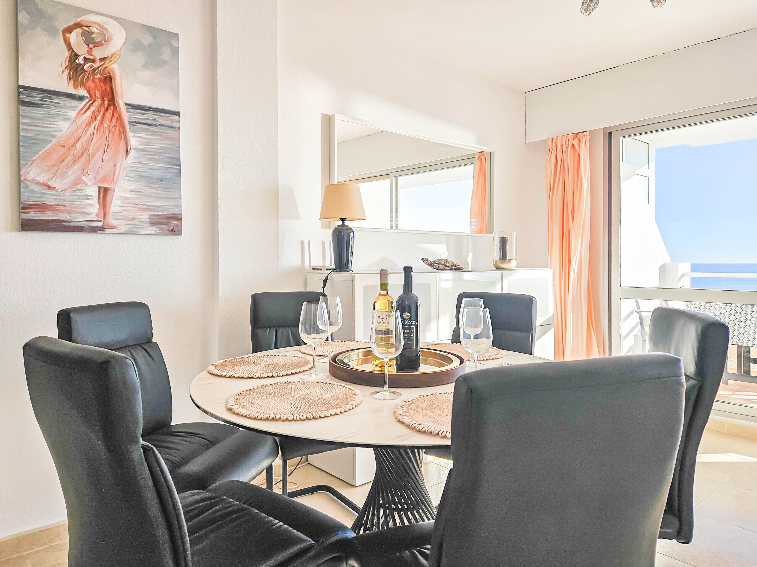 A dining area with a round table, black chairs, and a painting of a woman by the sea.