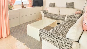 A living room with a sofa, coffee table, and a TV. There is a window with curtains and a painting on the wall. - Two bedroom apartment in Riviera del Sol (Mijas Costa)