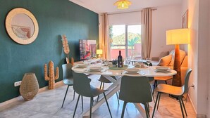 Un coin repas avec une table ronde dressée pour quatre personnes, entourée de chaises, d’un téléviseur et d’une bouteille de vin.