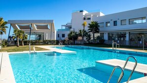 A swimming pool with clear blue water, surrounded by a white building with balconies and palm trees. - Three bedroom apartment in La Cala de Mijas (La Cala de Mijas)