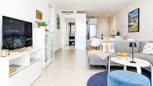 A modern living room with a TV, sofa, coffee table, and a blue ottoman. - Three bedroom apartment in La Cala de Mijas (La Cala de Mijas)