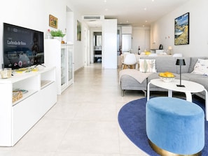 Uma sala de estar moderna com televisão, sofá, mesa de centro e um banquinho azul.