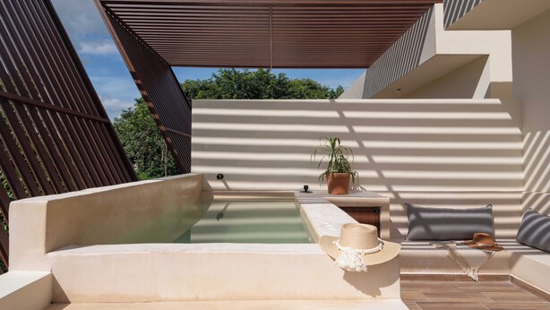 A modern outdoor seating area with a pool, a potted plant, and a hat on a cushion. - This villa is a 4 bedroom(s), 4 bathrooms, located in Tulum, QR. (Tulum)