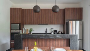 A modern kitchen with wooden cabinets, a granite countertop, and a dining area with a wooden table set for two. - This villa is a 4 bedroom(s), 4 bathrooms, located in Tulum, QR. (Tulum)