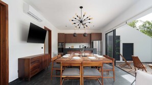 A modern dining area with a large wooden table set for six, surrounded by wooden chairs with grey cushions. A unique chandelier hangs above, and a flat-screen TV is mounted on the wall. - This villa is a 4 bedroom(s), 4 bathrooms, located in Tulum, QR. (Tulum)