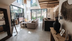 Un interior moderno con un amplio ventanal de arco, un sofá, una mesa de madera y una pared de piedra visible a través del ventanal.