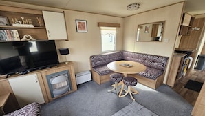 A compact RV interior with a sofa, a small table, a television, and a kitchenette. - Ty Mawr Chalet Sleeps 6 With Fireplace (Abergele)