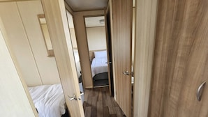 A narrow hallway with wooden doors leading to a bedroom with a bed and a bathroom. - Ty Mawr Chalet Sleeps 6 With Fireplace (Abergele)
