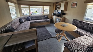A compact RV interior with a sofa set, a dining table, and a kitchenette. - Ty Mawr Chalet Sleeps 6 With Fireplace (Abergele)