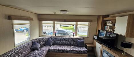 Un interior de autocaravana acogedor con un sofá modular, televisión y una pequeña cocina.