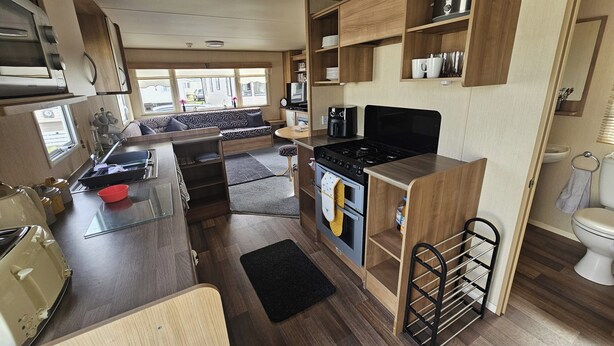 A compact RV kitchen with a stove, sink, and a dining area with a bench. - Ty Mawr Chalet Sleeps 6 With Fireplace (Abergele)