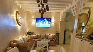 A modern living room with a sofa, TV, and dining area with a table and chairs. - Dar Malika (El Jadida)