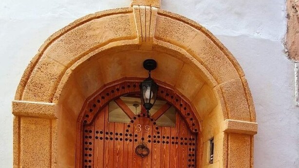 A wooden door with a decorative metal grille, set within an arched stone frame. - Dar Malika (El Jadida)