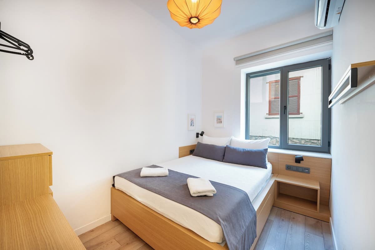 Un dormitorio moderno con cama, mesitas de noche, una ventana con contraventanas y una lámpara colgante.