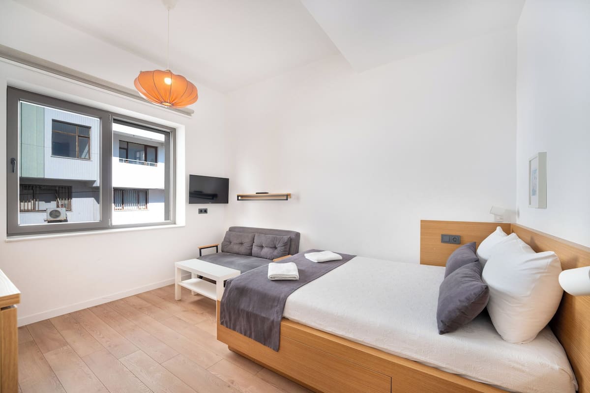 Un dormitorio moderno con cama, mesita de noche y ventana con vistas a edificios.