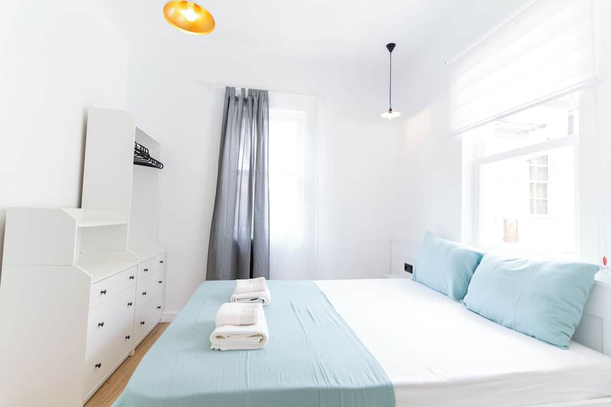 Una habitación de hotel con una cama, un tocador blanco, una ventana con cortinas y una lámpara en el techo.