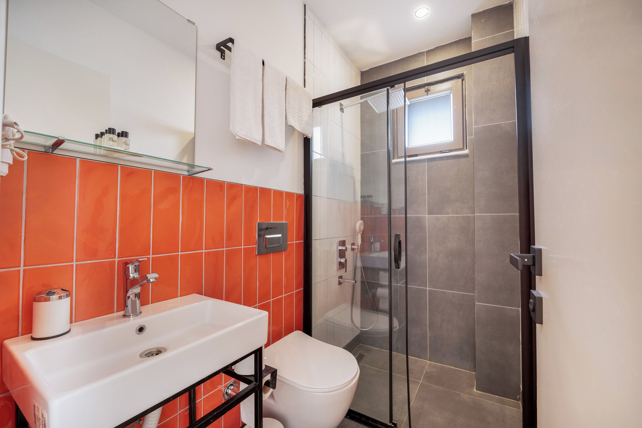 A bathroom with a glass-enclosed shower, a white sink, and orange-tiled walls.