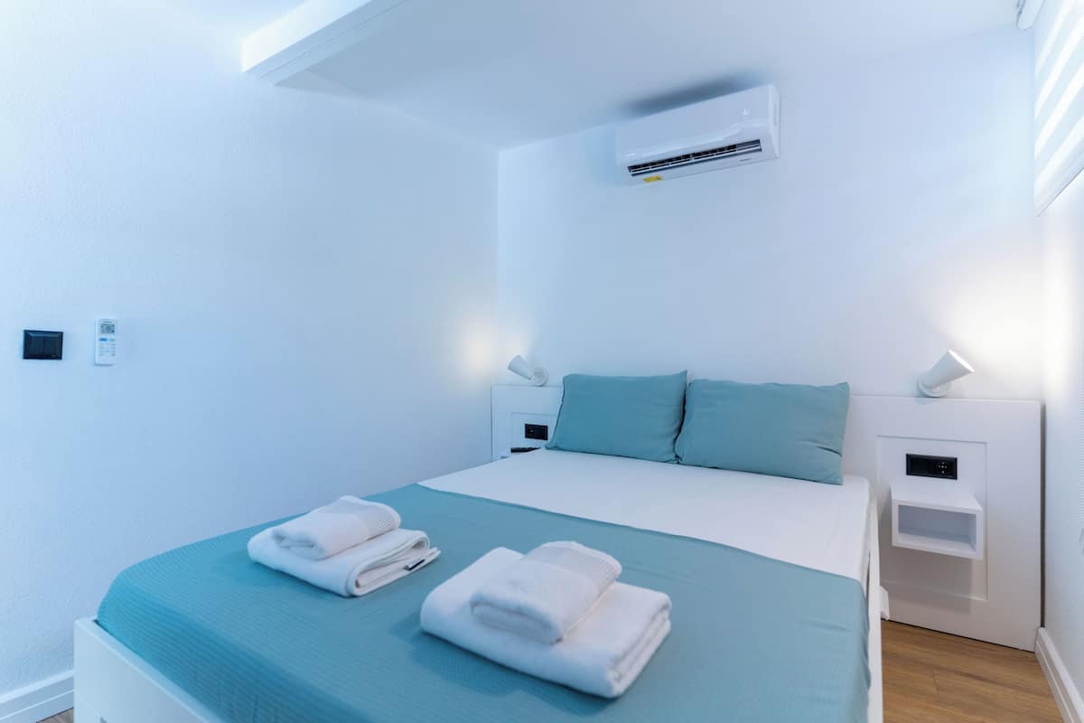 Una habitación de hotel moderna con una cama grande, dos mesitas de noche, un equipo de aire acondicionado y un panel de control en la pared.
