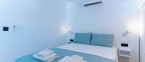 A modern hotel room with a large bed, two bedside tables, an air conditioning unit, and a wall-mounted control panel.