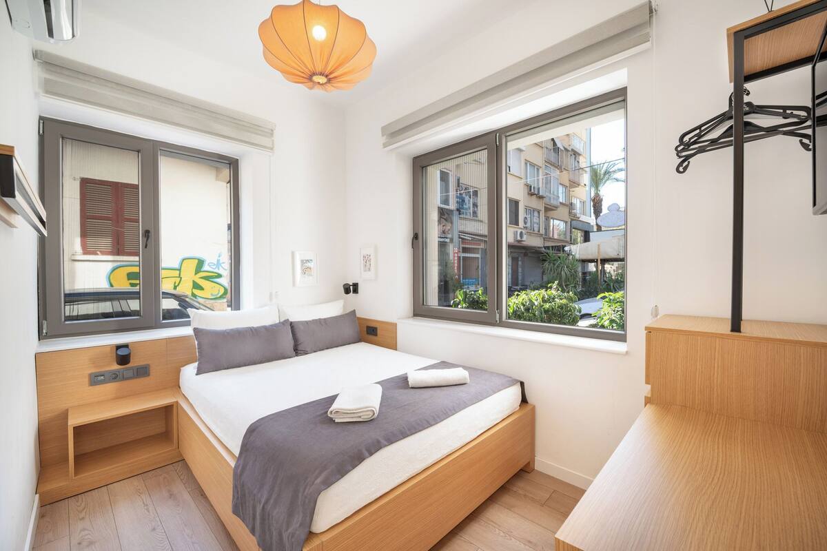 Un dormitorio moderno con cama, mesitas de noche, lámpara colgante y ventanas amplias que ofrecen vistas al exterior.