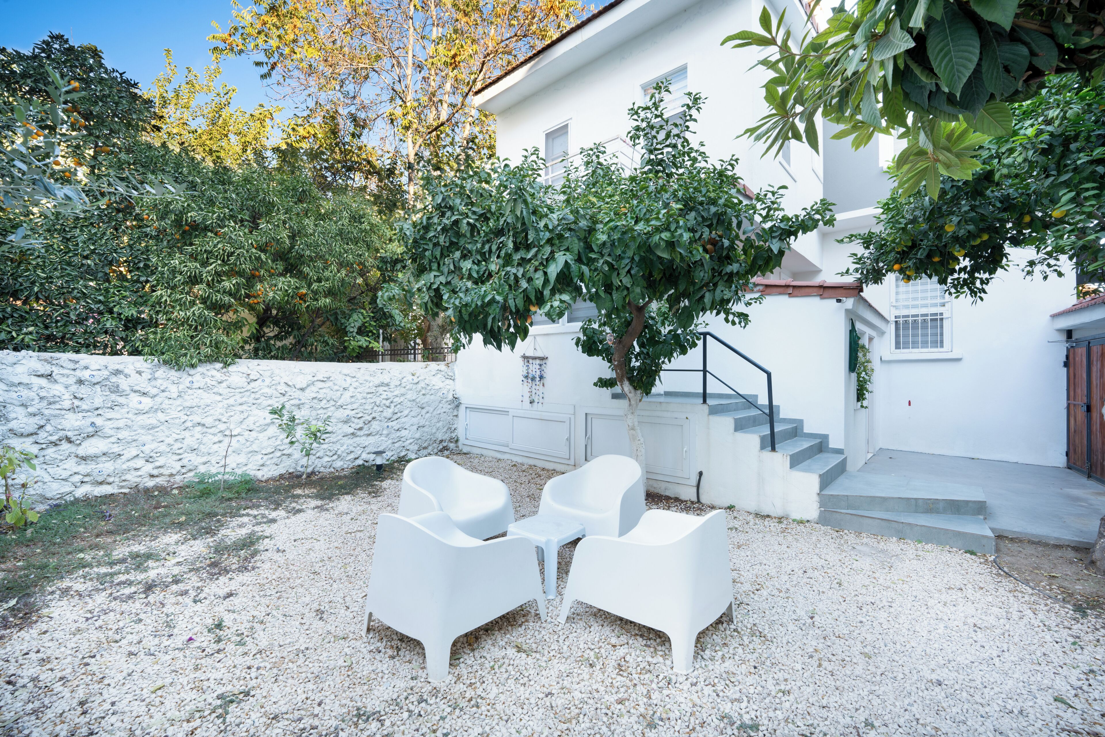A white building with a staircase, a tree, and white outdoor furniture.