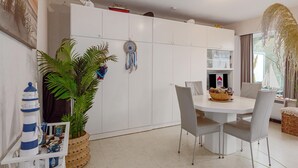 Een moderne eetruimte met een witte tafel, grijze stoelen, een potplant en een dromenvanger aan de muur.