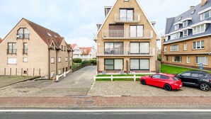 Een woongebouw met een puntig dak, een balkon op de tweede verdieping en een geplaveid oprit.