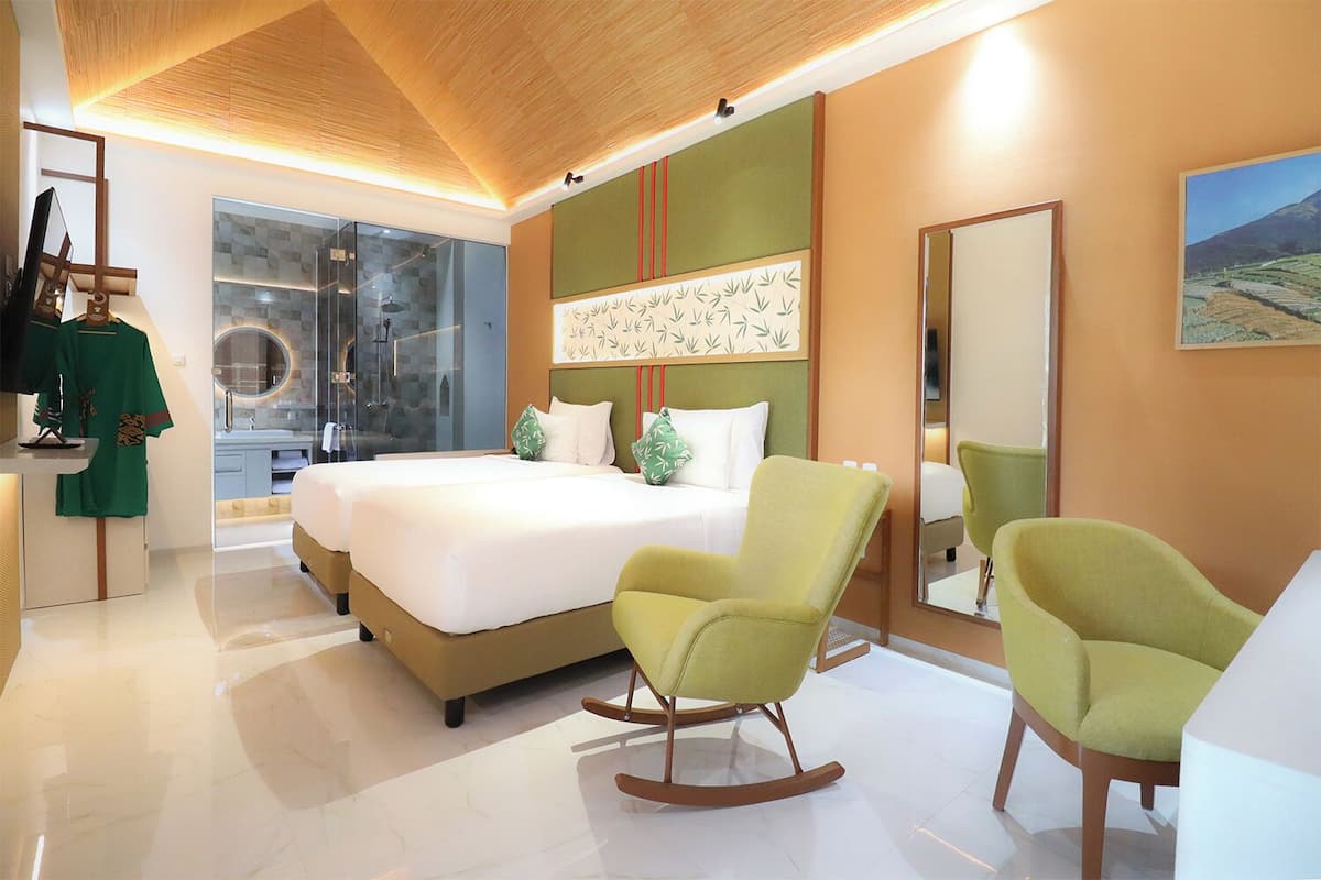 A modern hotel room with a large bed, two rocking chairs, a glass shower, and a green and beige color scheme.