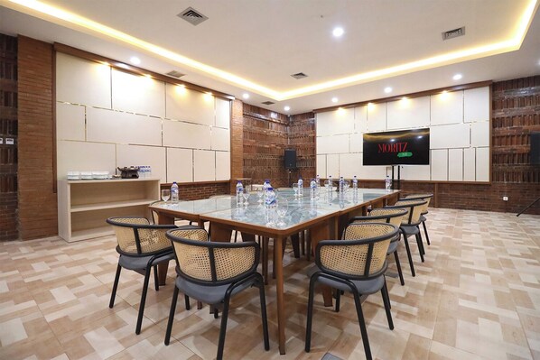 Un salón de conferencias con una larga mesa, sillas, botellas de agua y una pantalla de televisión que muestra 'MORITZ'.