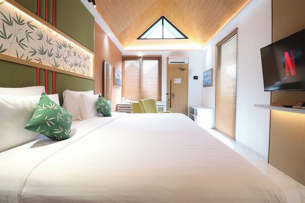 A hotel room with a large bed, a TV mounted on the wall, a ceiling with a skylight, and a wall with a bamboo leaf pattern.