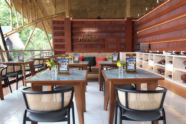A restaurant with a traditional Indonesian design, featuring bamboo structures, wooden tables, and rattan chairs.