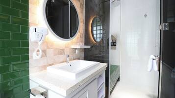 Une salle de bain moderne avec un lavabo blanc, deux miroirs ronds, une douche en verre et un mur recouvert de carreaux verts.
