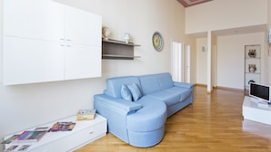 A living room with a blue sectional sofa, white cabinets, and a television on a white stand. - Four canti luxury apartment  (Palermo)