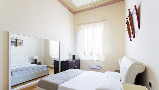 A modern bedroom with a large bed, bedside tables, a wardrobe, and a mirror. - Four canti luxury apartment  (Palermo)