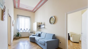 A living room with a blue sofa, a white armchair, a small table, and a potted plant. - Four canti luxury apartment  (Palermo)