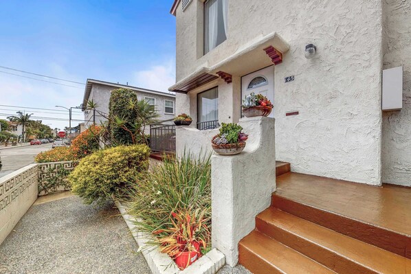 A house with a white stucco exterior, a front porch with steps, and potted plants.