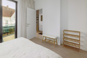 A bedroom with a large bed, a wooden bench, a multi-tiered shelf, and a view of the outside.