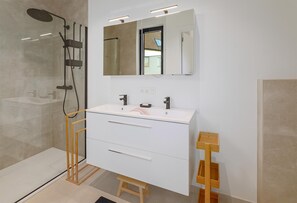 A modern bathroom with a glass-enclosed shower, a white vanity with a mirror, and a wooden stool.