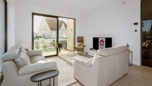 Ein modernes Wohnzimmer mit einem weißen Sofa, einem Glastisch und einem Fernseher auf einem Lowboard.