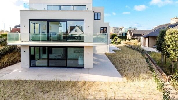 Ein modernes, zweistöckiges Haus mit großen Glasfenstern und einem Balkon.