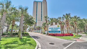 Naamplaatje voor Sand Dunes Resort, met een hoog gebouw op de achtergrond.