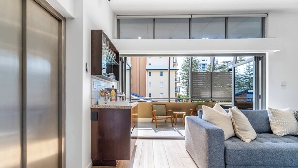 Ein modernes Wohnzimmer mit grauem Sofa, Holzboden und Blick auf den Balkon.